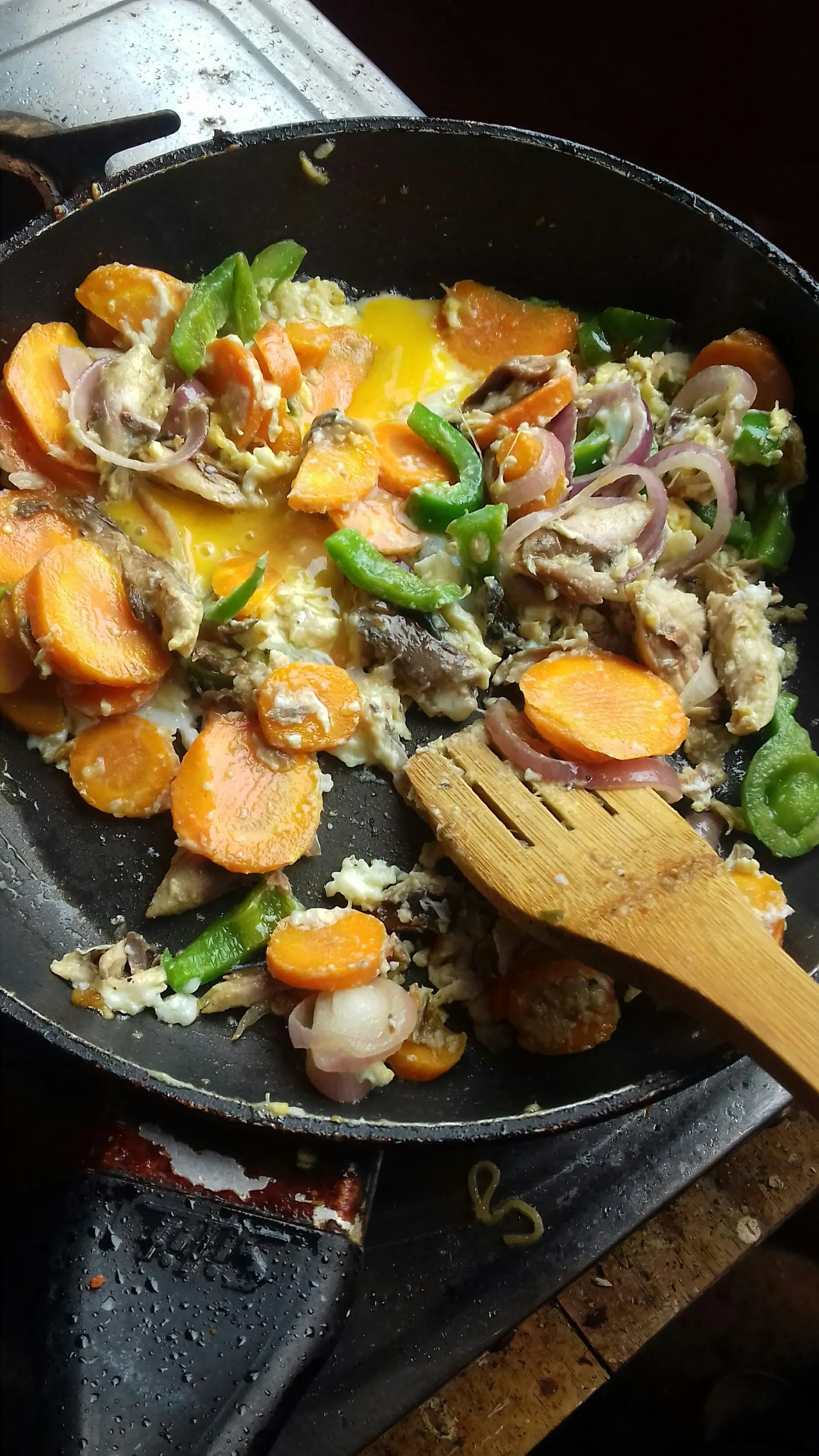 Eggs cooking with sliced carrots, green peppers, mushrooms, and onions in a black pan